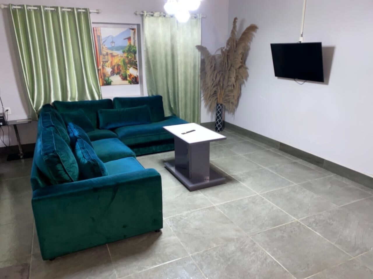 A room with a teal sectional sofa, a small grey table, a mounted TV, and a door with a view of a landscape.