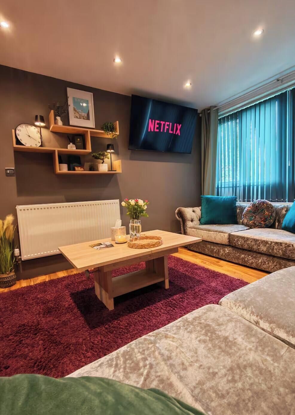 A modern living room with a flat-screen TV displaying 'NETFLIX,' a wooden coffee table, a sofa, and a radiator.