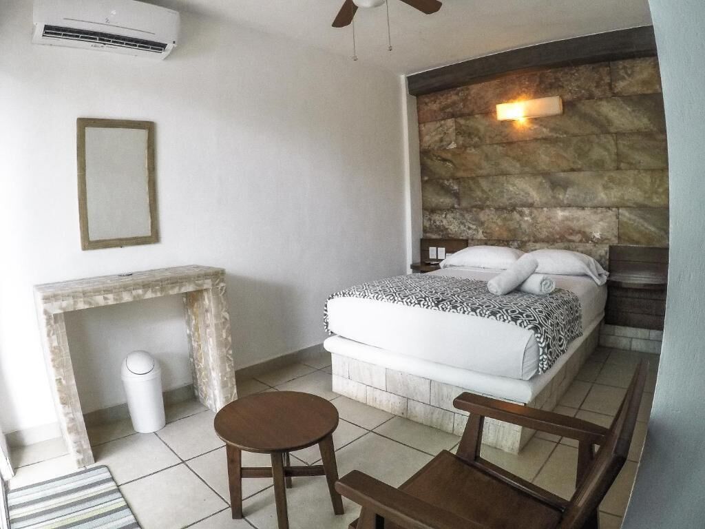 A bedroom with a bed, a small table, a chair, a trash bin, and a wall-mounted air conditioner.