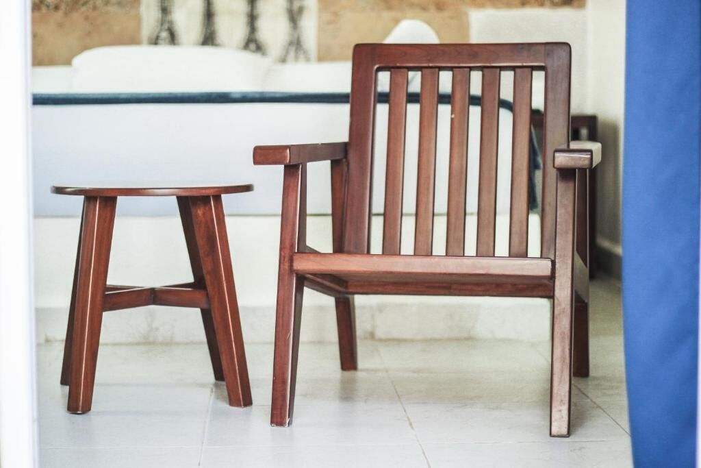 Una silla de madera y una pequeña mesa redonda en una habitación con una bañera blanca al fondo.