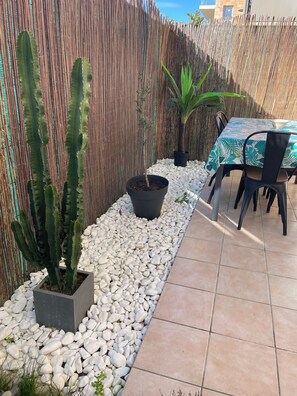 A patio area with a tiled floor, white pebbles, a bamboo fence, and a table with chairs. - LE NID PROVENÇAL - Ground-floor apartment with garden, pool, and terrace (Le Pontet)