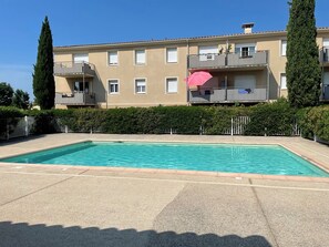 A rectangular swimming pool with a paved deck, surrounded by a low hedge and a metal fence. - LE NID PROVENÇAL - Ground-floor apartment with garden, pool, and terrace (Le Pontet)