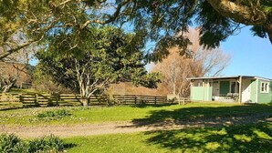 A green house with a porch, surrounded by a fenced yard and trees. - Hilltop farm cabin, private deck & sweeping views, 10 mins to Ōhope Beach (Wainui)