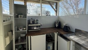 A compact kitchen with a microwave, toaster, and kettle on the counter, a small refrigerator, and a window with a view of trees. - Hilltop farm cabin, private deck & sweeping views, 10 mins to Ōhope Beach (Wainui)