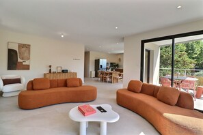 A modern living room with two orange sofas, a white coffee table, and a dining area in the background. - Villa Nova – Maison neuve, piscine & confort (Ventabren)