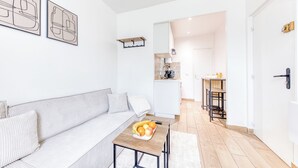 En moderne stue med en sofa, et sofabord med frugt, og et køkken i baggrunden.
