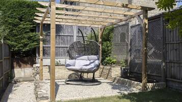 A wooden pergola with a hanging chair, stone walls, and a fenced garden area.