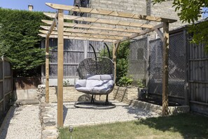 Una pergola in legno con una sedia a dondolo, pareti in pietra e un'area giardino recintata.