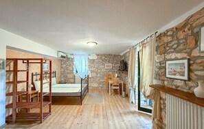 A room with a bed, a wooden chair, a table, a stone wall, and a radiator. - Awesome home in Marcana (Marcana)