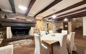 Une cheminée en pierre avec un manteau noir, une table ronde en bois entourée de chaises blanches, et un panneau indiquant « PRIVÉ » sur le mur.