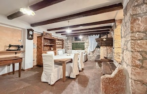 A rustic room with exposed beams, stone walls, a wooden table with chairs, and a vintage sewing machine. - Awesome home in Marcana (Marcana)