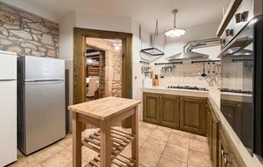 A kitchen with a stone wall, wooden cabinets, a built-in oven, and a wooden table. - Awesome home in Marcana (Marcana)