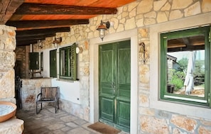 A stone-walled corridor with a bench, a green door, and a window with a view of the outside. - Awesome home in Marcana (Marcana)