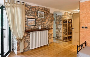 Une pièce aux murs de pierre, avec un plancher en bois, un radiateur, un lit, une armoire et une étagère remplie d’objets.