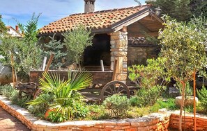 A rustic stone building with a tiled roof, surrounded by greenery and a wooden cart. - Awesome home in Marcana (Marcana)
