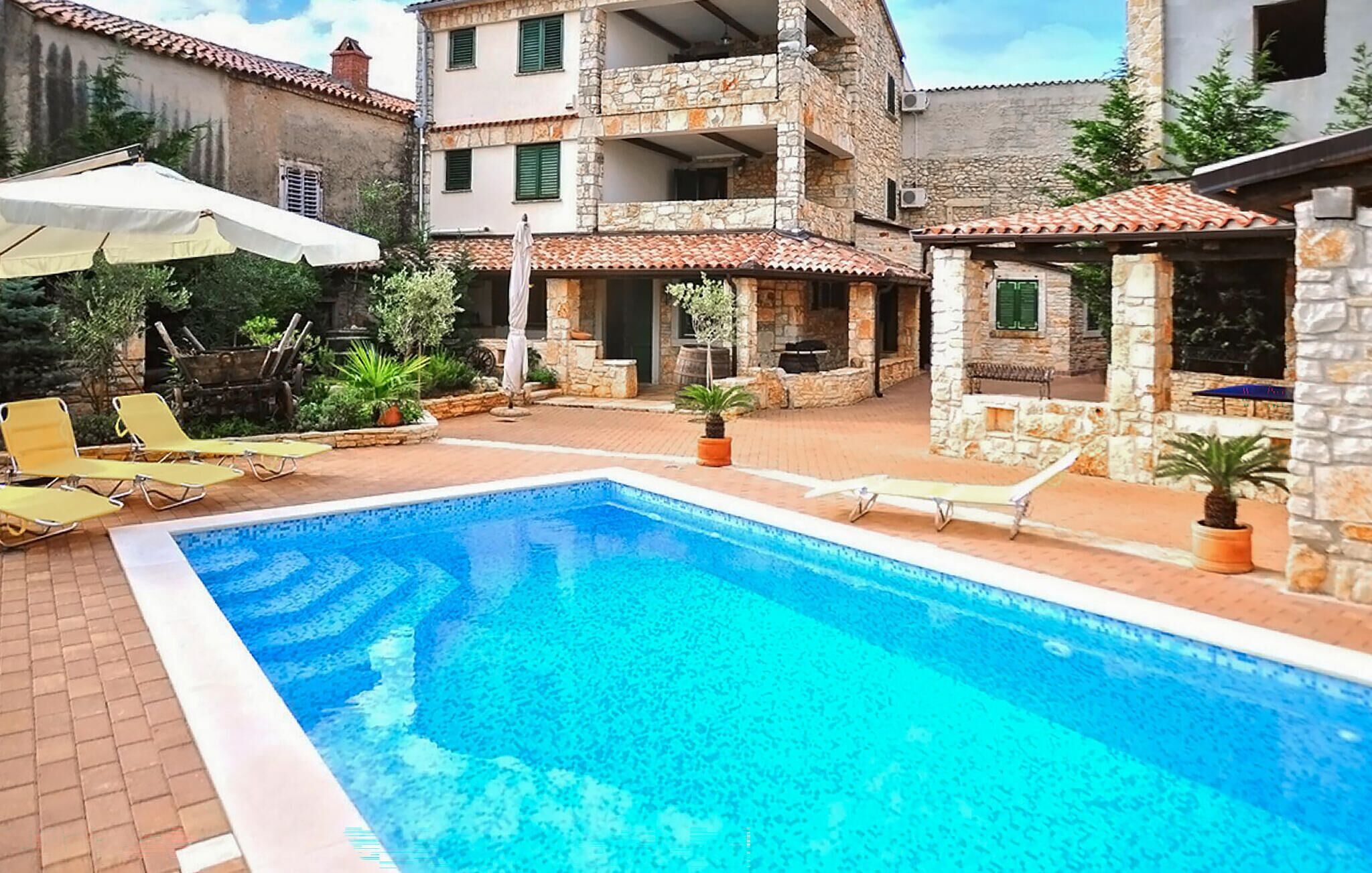 Une piscine entourée de bâtiments en pierre dotés de balcons, avec des chaises longues et des parasols à proximité.