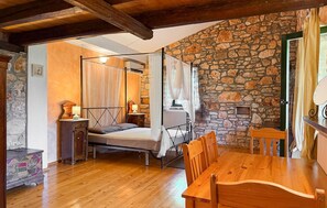 A bedroom with a four-poster bed, stone wall, wooden floor, and a dining area with a table and chairs. - Awesome home in Marcana (Marcana)