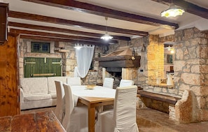 A rustic interior with a stone fireplace, wooden beams, and a dining area with white upholstered chairs. - Awesome home in Marcana (Marcana)