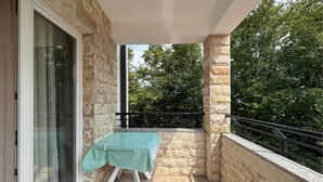 A balcony with a table covered by a green cloth, stone walls, and a view of trees. - Stunning apartment in Pula with swimming pool (Pula)