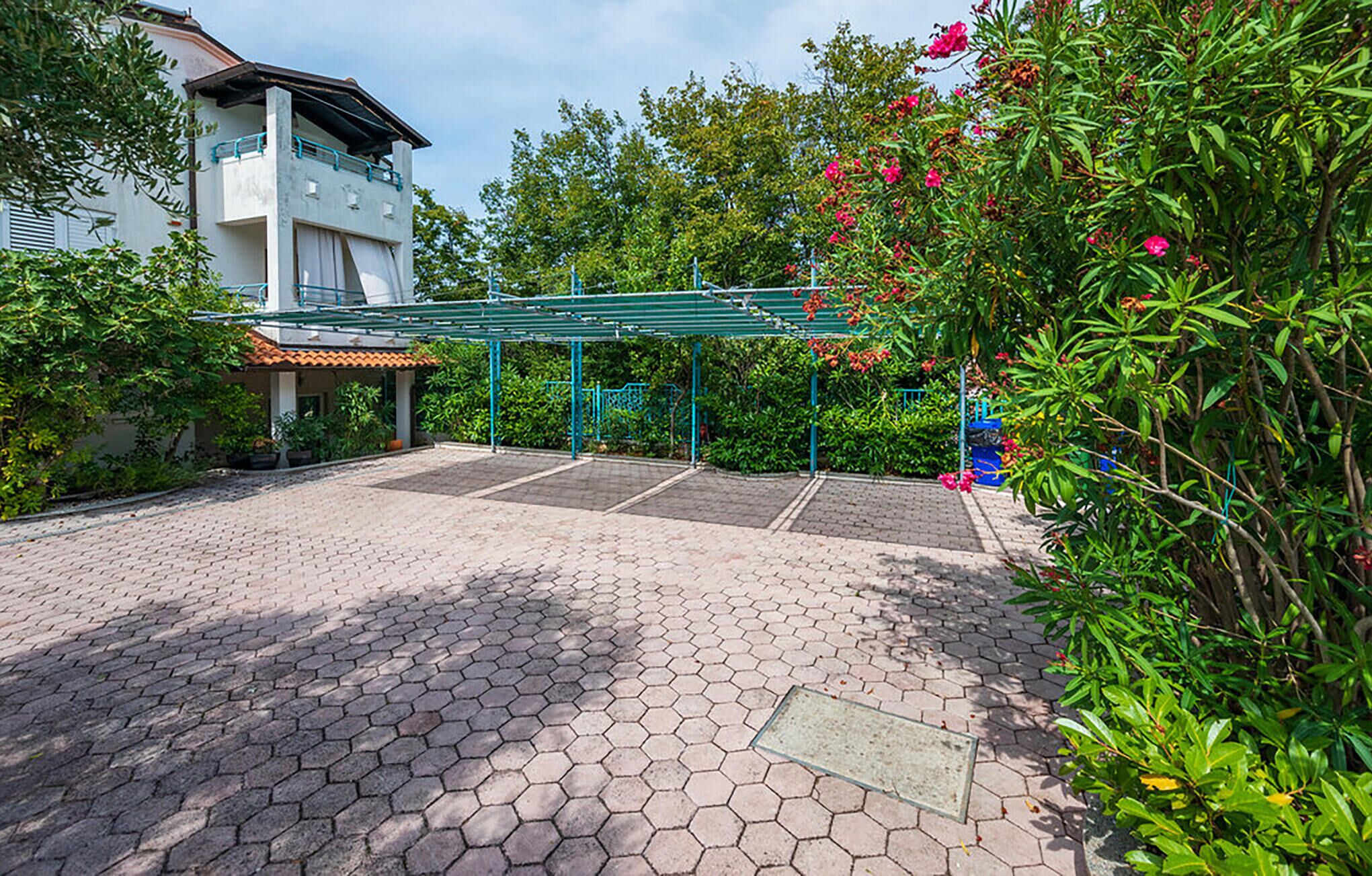 A paved outdoor area with a covered seating area, surrounded by greenery and a building with a balcony.