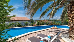 A swimming pool with lounge chairs, palm trees, and a tiled patio area. - Stunning apartment in Pula with swimming pool (Pula)