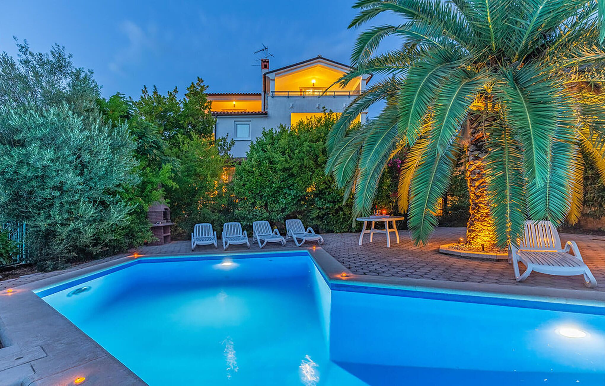 A swimming pool with lounge chairs and a house in the background.