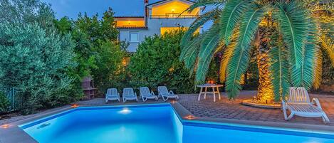 A swimming pool with lounge chairs and a house in the background.