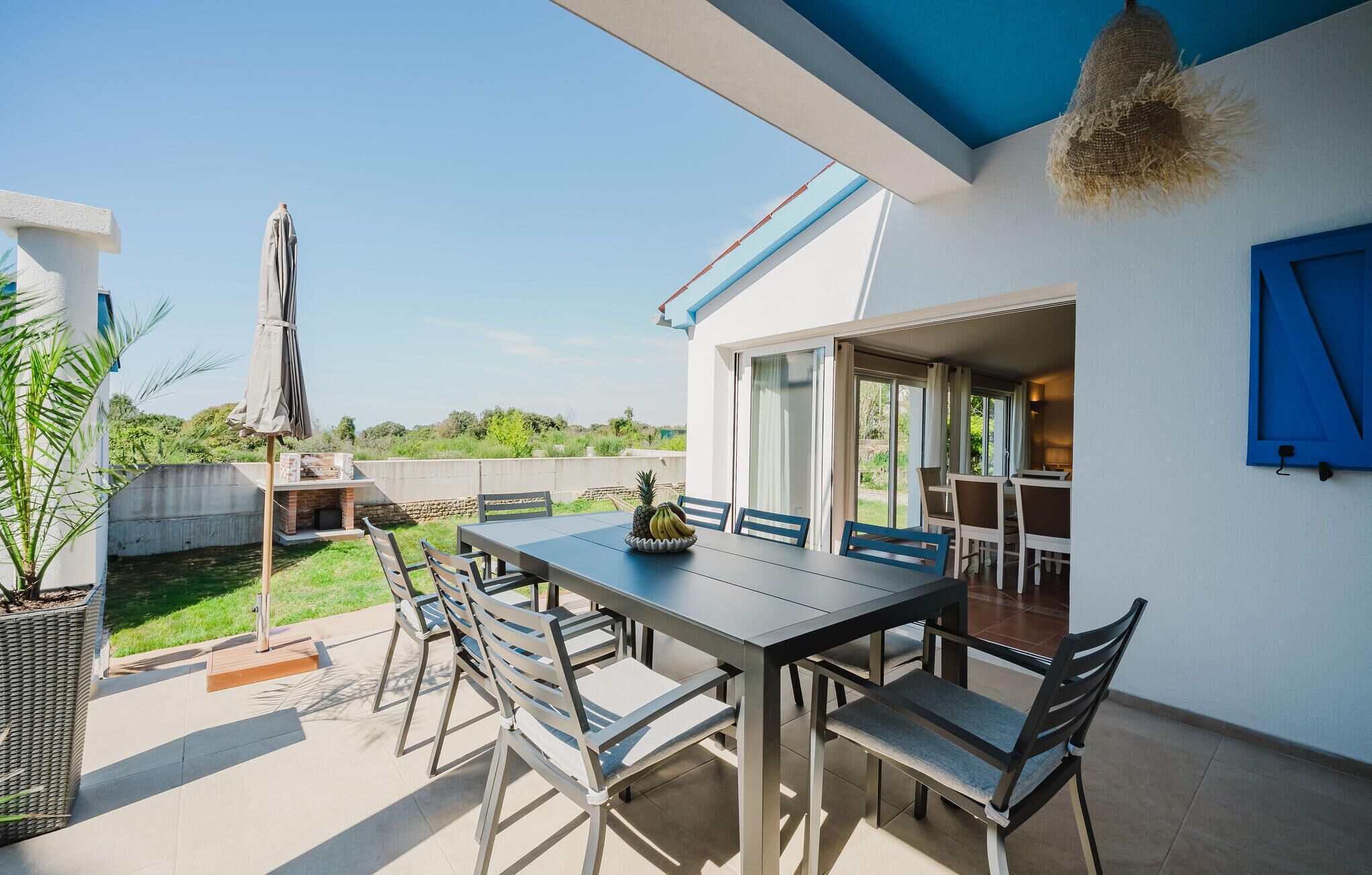 Une terrasse extérieure avec une table et des chaises, un luminaire suspendu et une vue sur le paysage environnant.