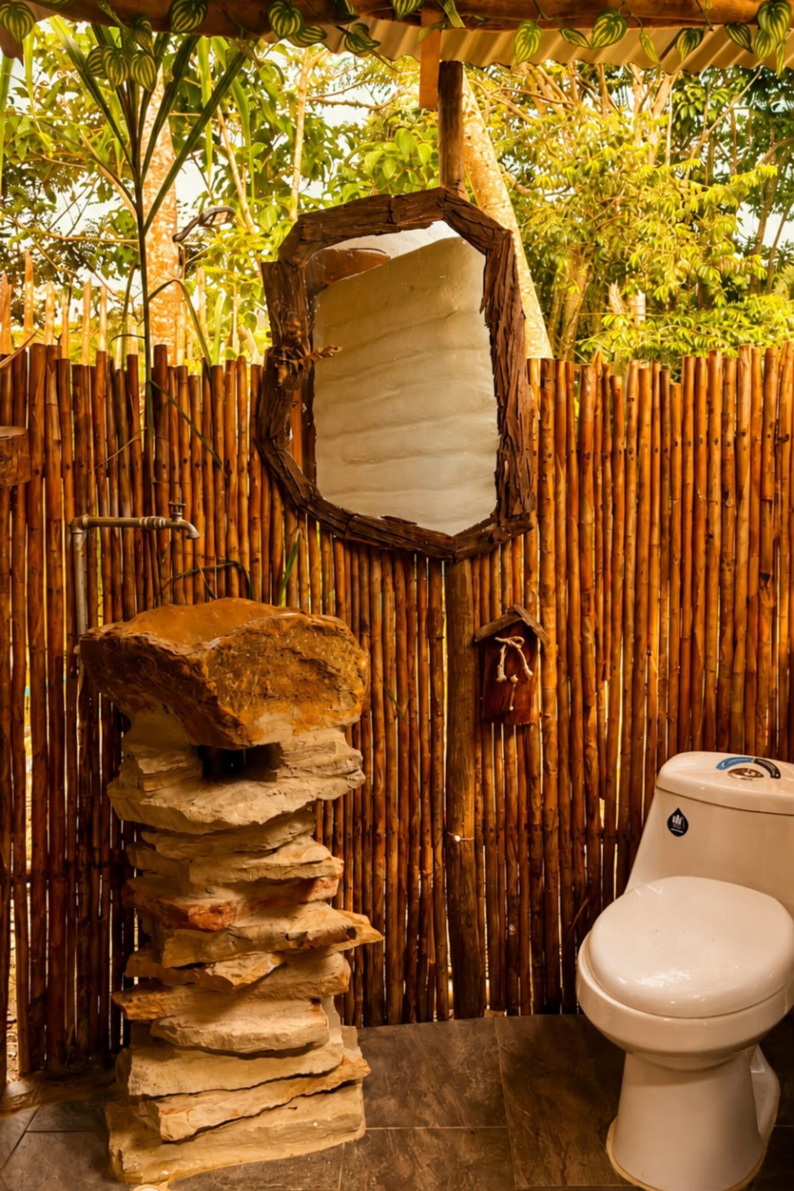 Un baño rústico con pared de bambú, lavabo de piedra y un inodoro.
