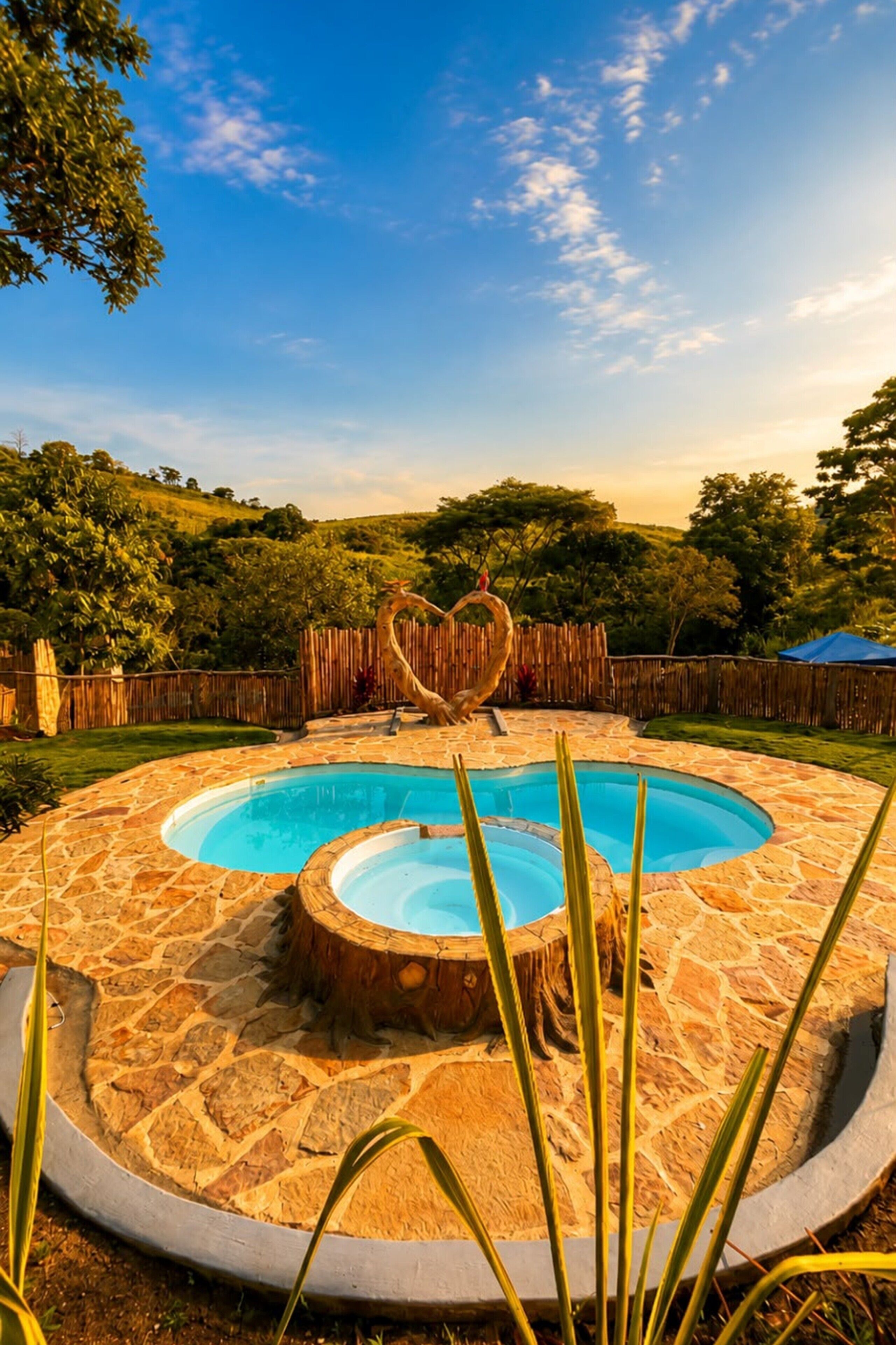 A circular stone pool with a heart-shaped decoration in the center, surrounded by a wooden fence and trees.