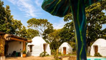 A mushroom-shaped sculpture in a courtyard with white dome-shaped buildings and a pool in the background.
