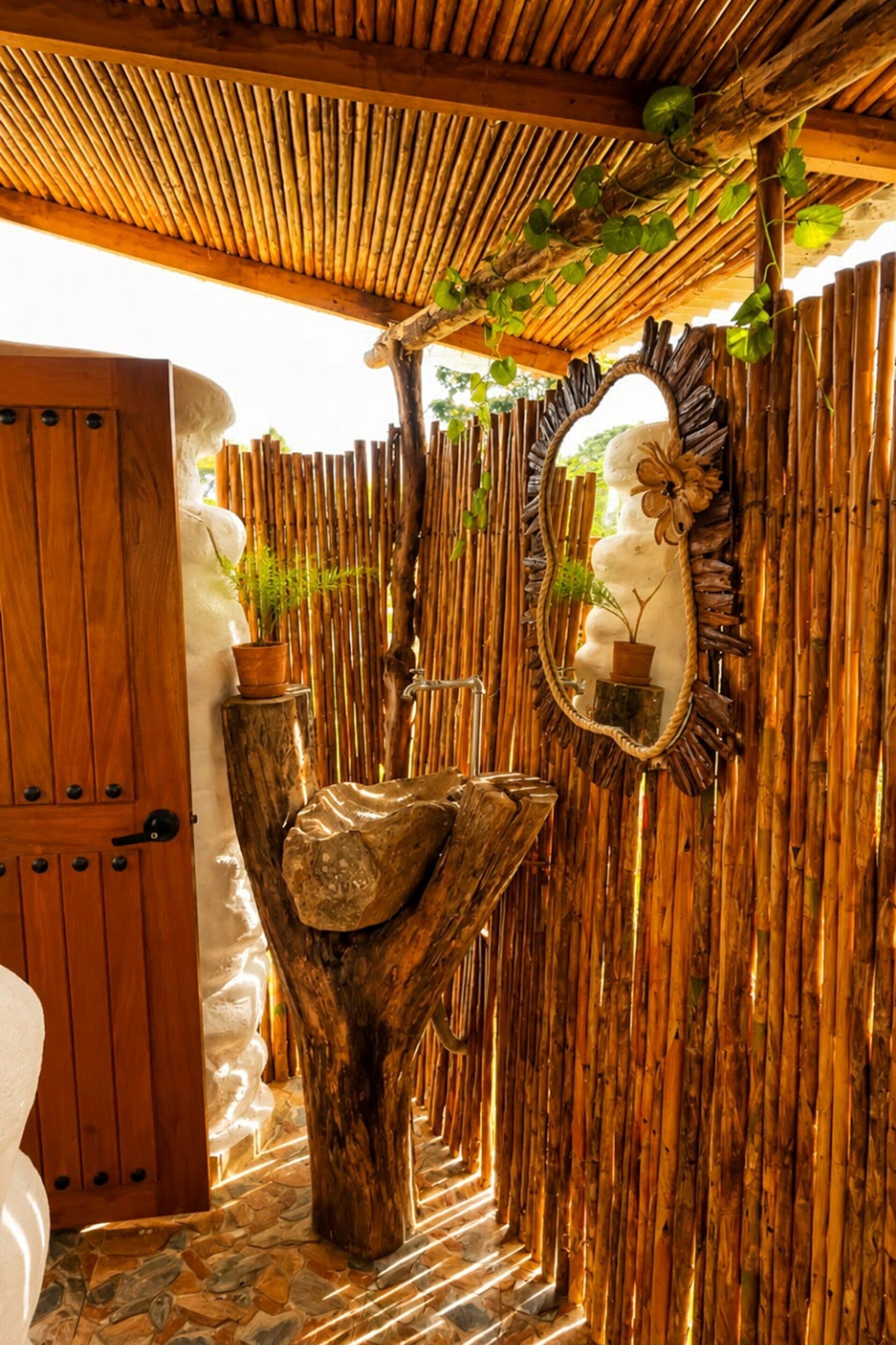 Una porta in legno, un lavandino in pietra, uno specchio e una parete di bambù.
