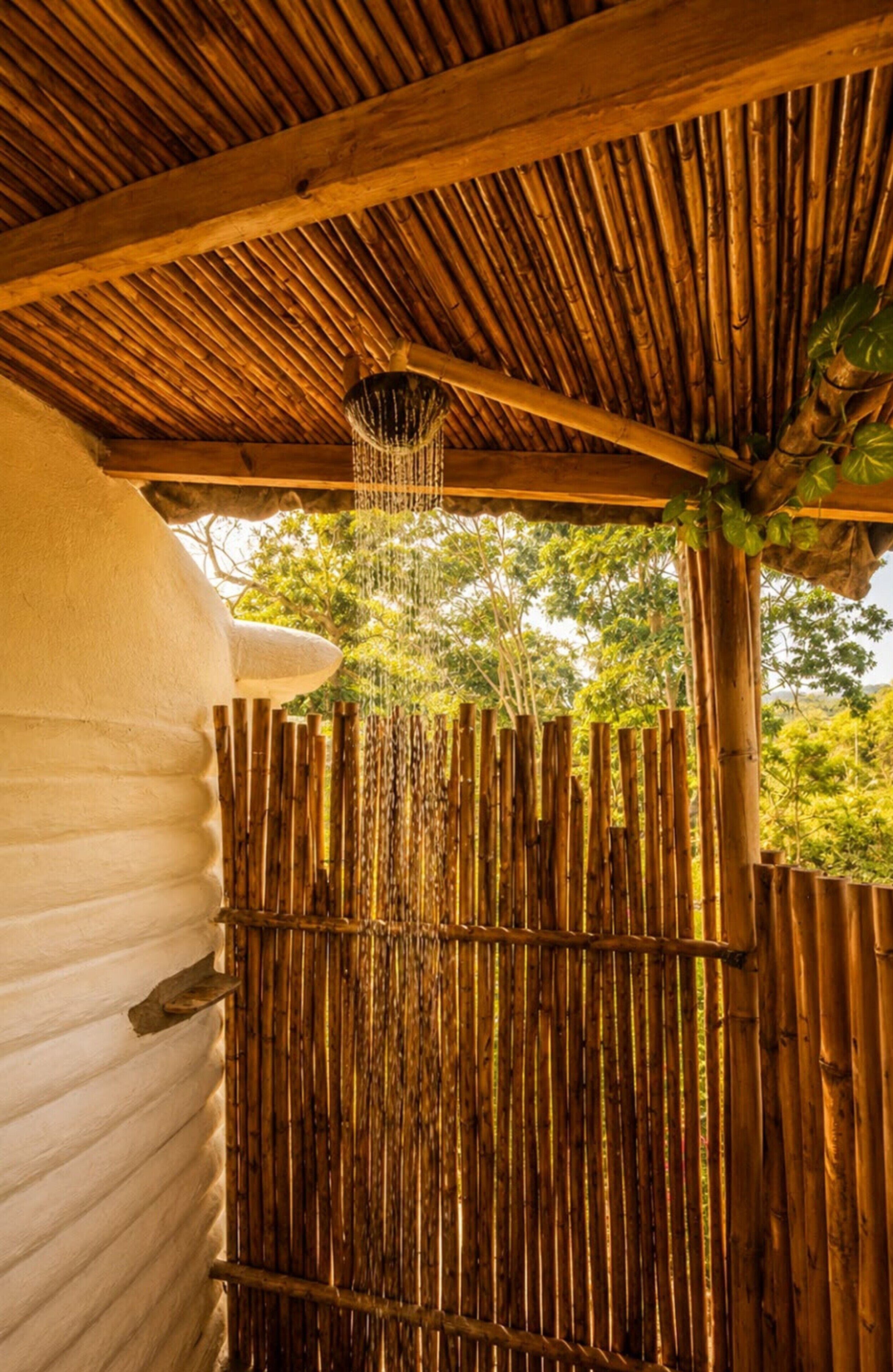 Una estructura de bambú con una fuente colgante, una pared blanca y vistas al follaje.