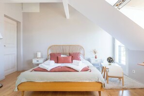 Ein Schlafzimmer mit schrägem Dach, einem Bett mit rosa und weißer Bettwäsche, einem Nachttisch mit Lampe, einem Globus und einem Sessel.