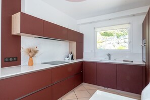 Eine moderne Küche mit Fenster, weißen Arbeitsplatten und roten Schränken.