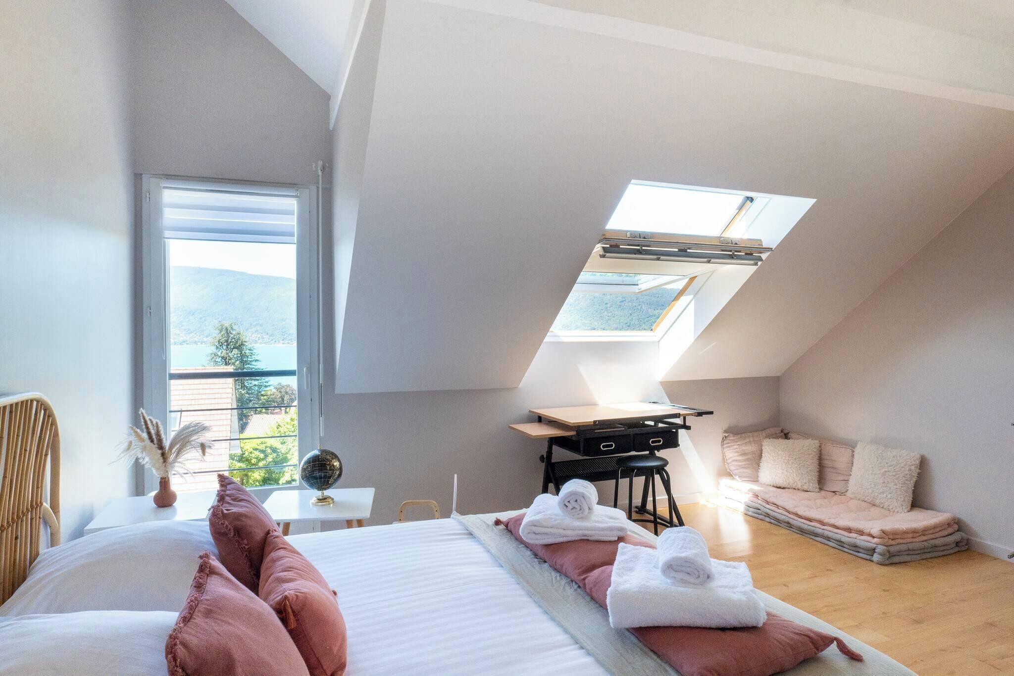 Une chambre moderne avec un puits de lumière, un lit agrémenté d’oreillers roses, un bureau avec un globe terrestre et une vue sur l’extérieur.