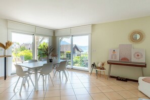 Ein geräumiger Essbereich mit einem großen Tisch und Stühlen, Blick auf Grünflächen und Berge durch große Fenster sowie eine Wand mit gerahmten Kunstwerken.
