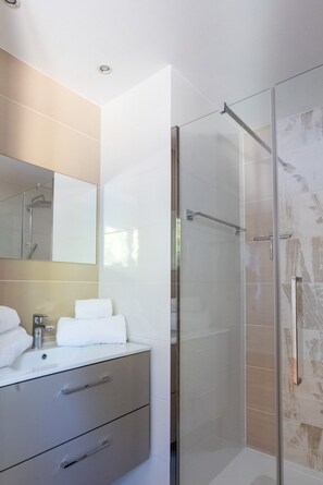 Ein modernes Badezimmer mit einer Duschkabine aus Glas, einem weißen Waschbecken mit Spiegel darüber und einer beige gefliesten Wand.