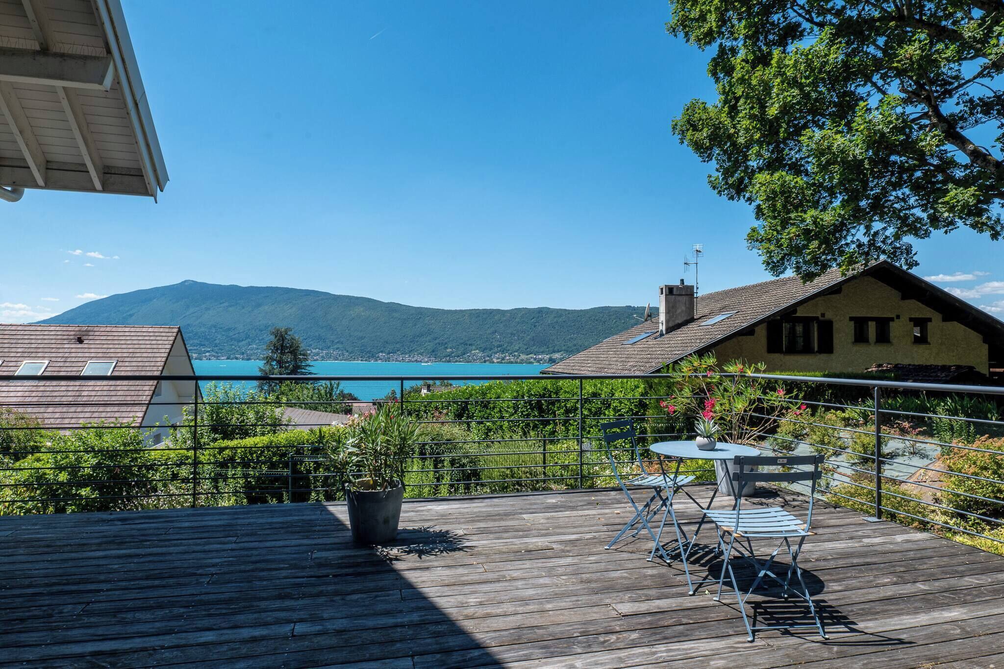 A wooden deck with a table and chairs, overlooking a body of water and mountains.