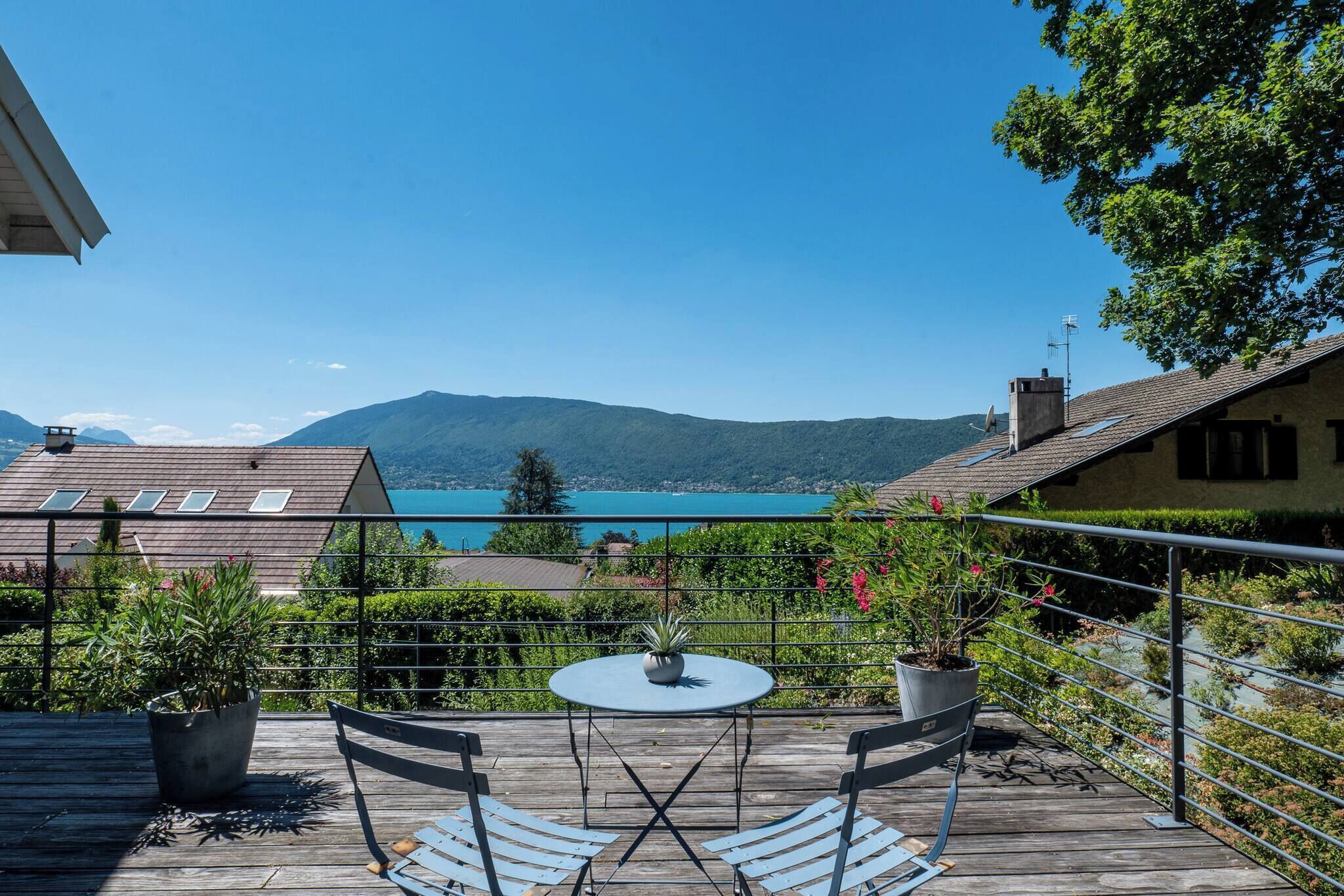 Une terrasse en bois avec une table et des chaises, offrant une vue sur un lac et des montagnes.