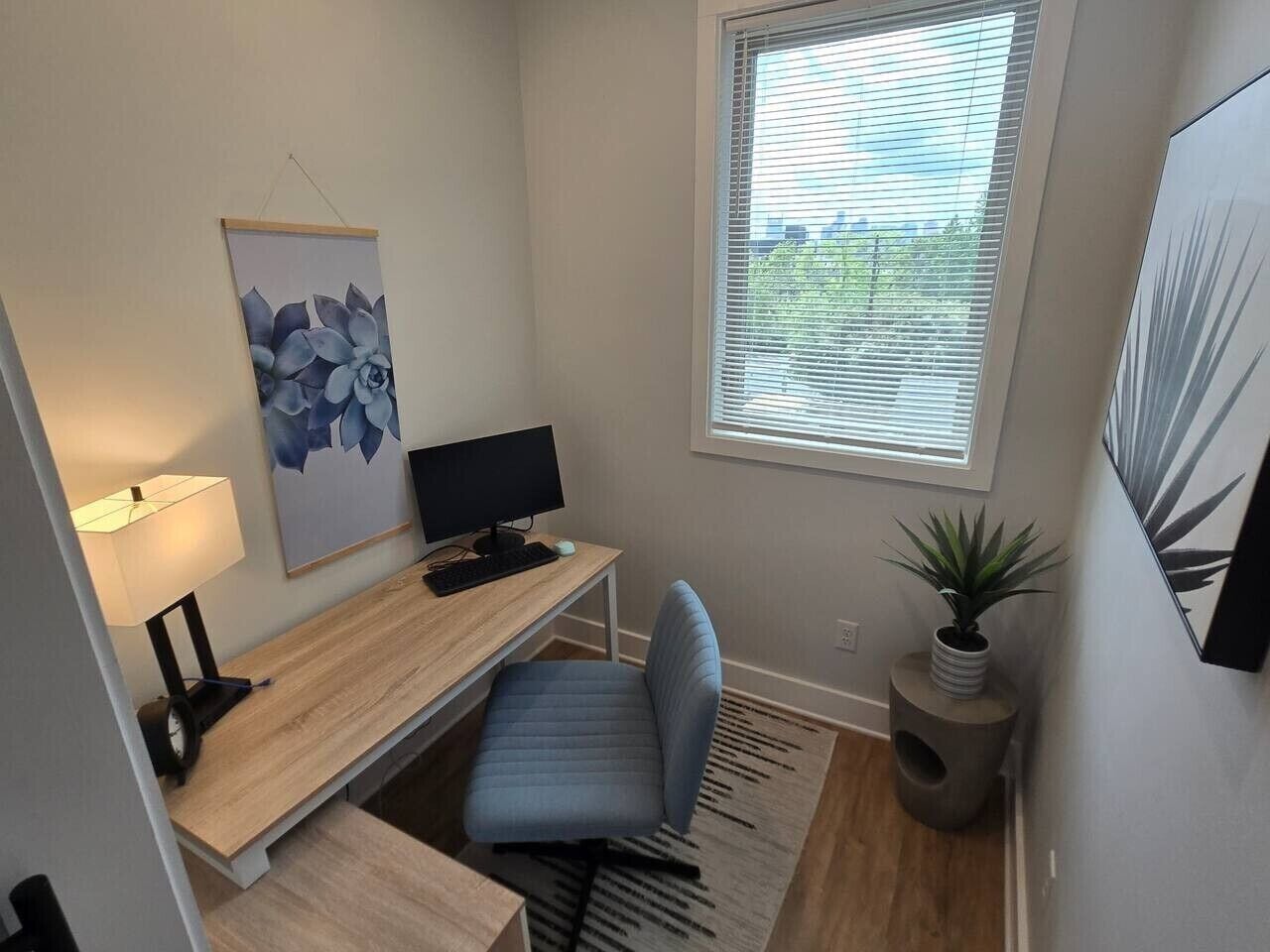 Un pequeño espacio de oficina con un escritorio, una silla, una computadora, una lámpara y una ventana con persianas.