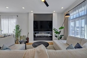 A modern living room with a sofa set, a coffee table, and a TV. There is a plant and a guitar in the room. - 14 Room, 27 bed, Multi-Townhome Complex, Roof Decks, 2mi to DT! (Nashville)
