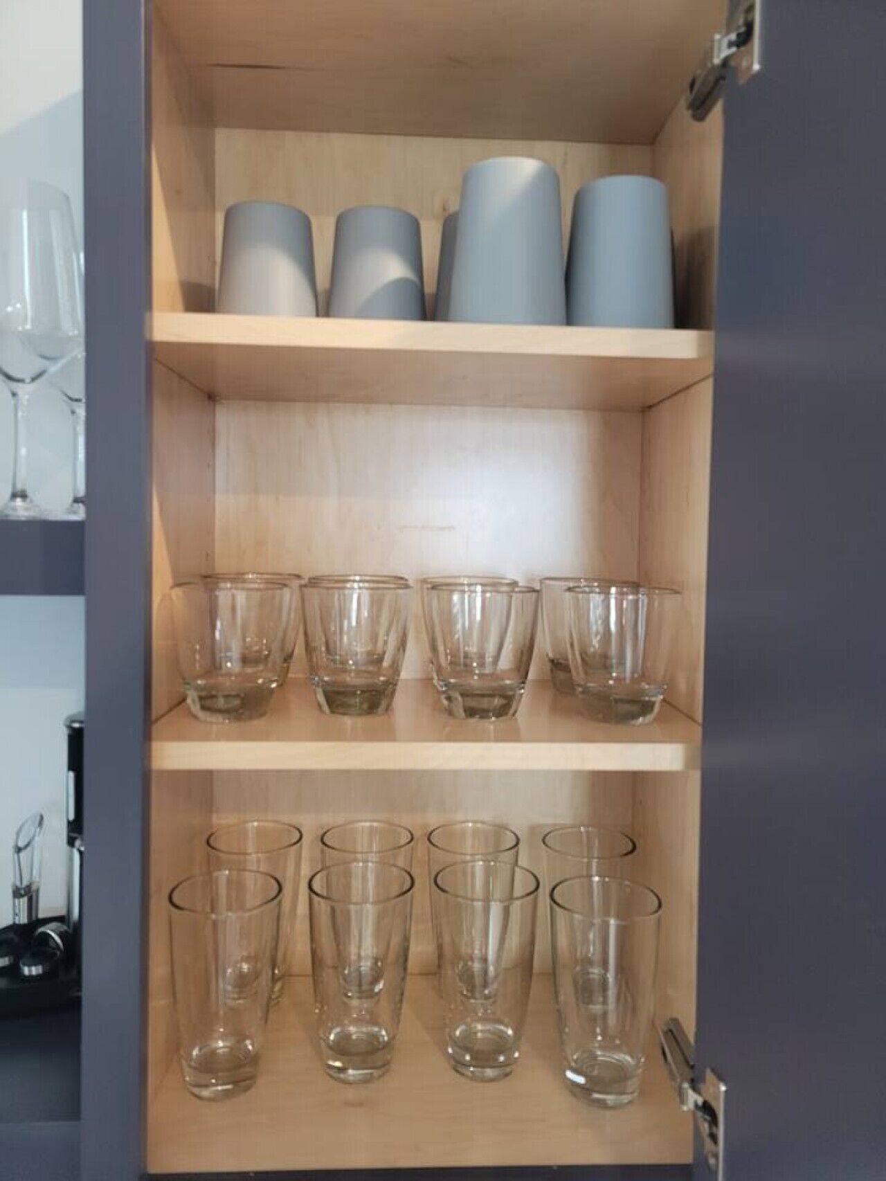 Een houten kast met planken met helder glazen servies en enkele metalen bakken.