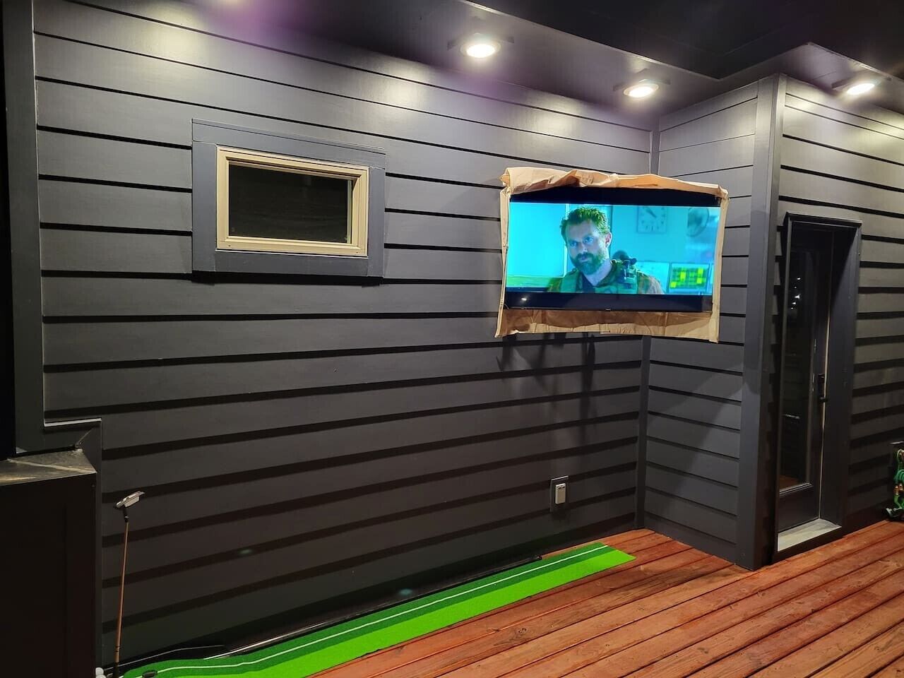 A room with dark wooden walls, a mounted television, and a wooden floor.