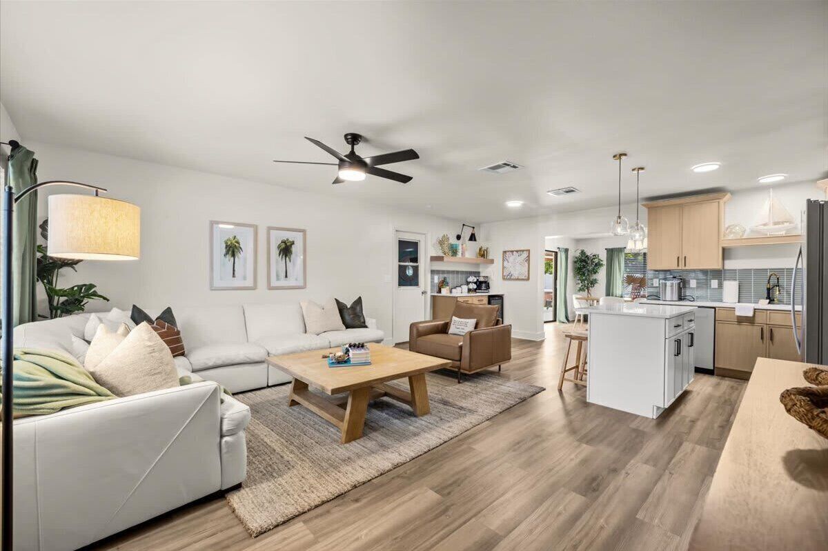 A modern living room with a sofa, coffee table, and a dining area with a kitchen in the background.