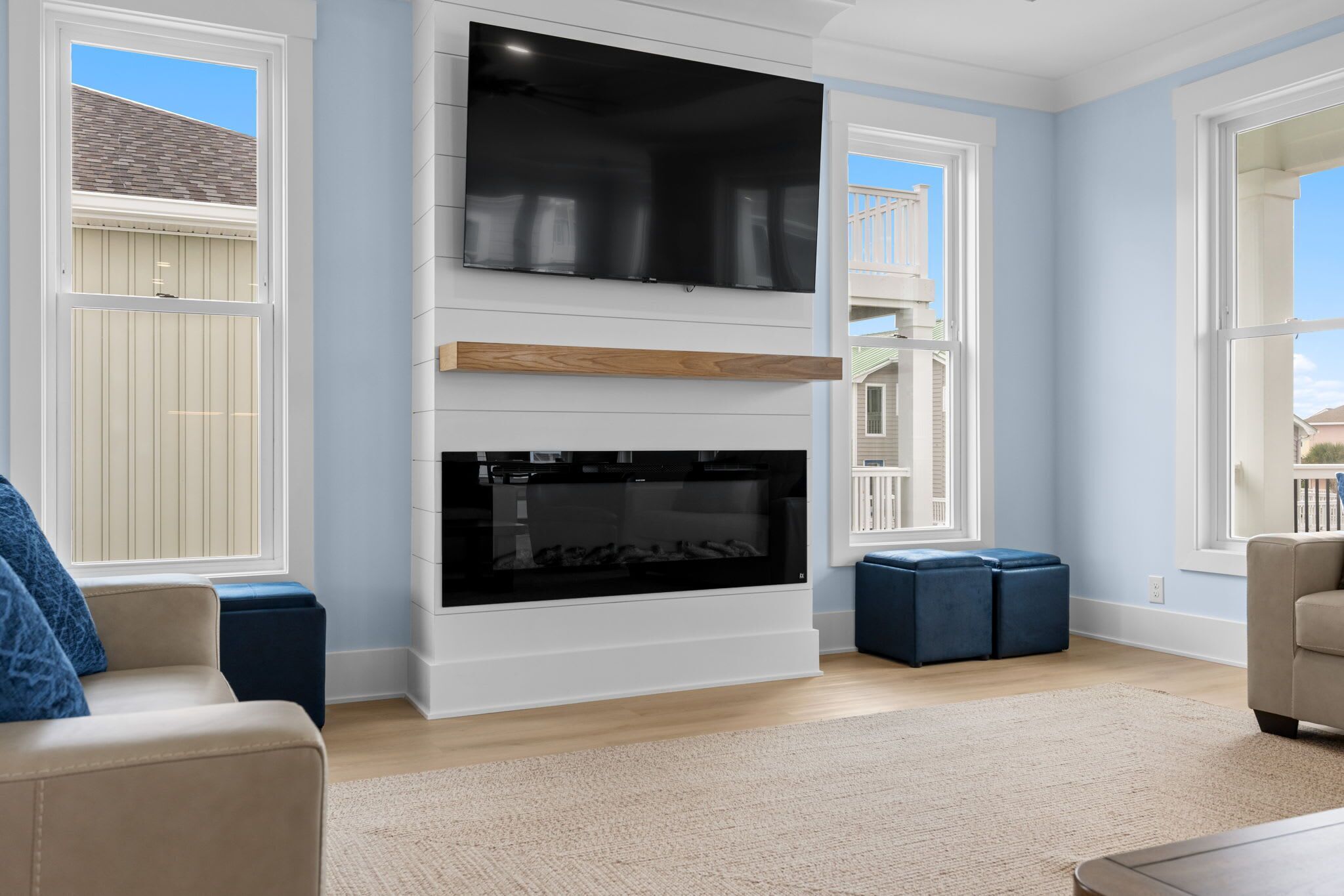 A living room with a fireplace, a TV mounted above it, and large windows.