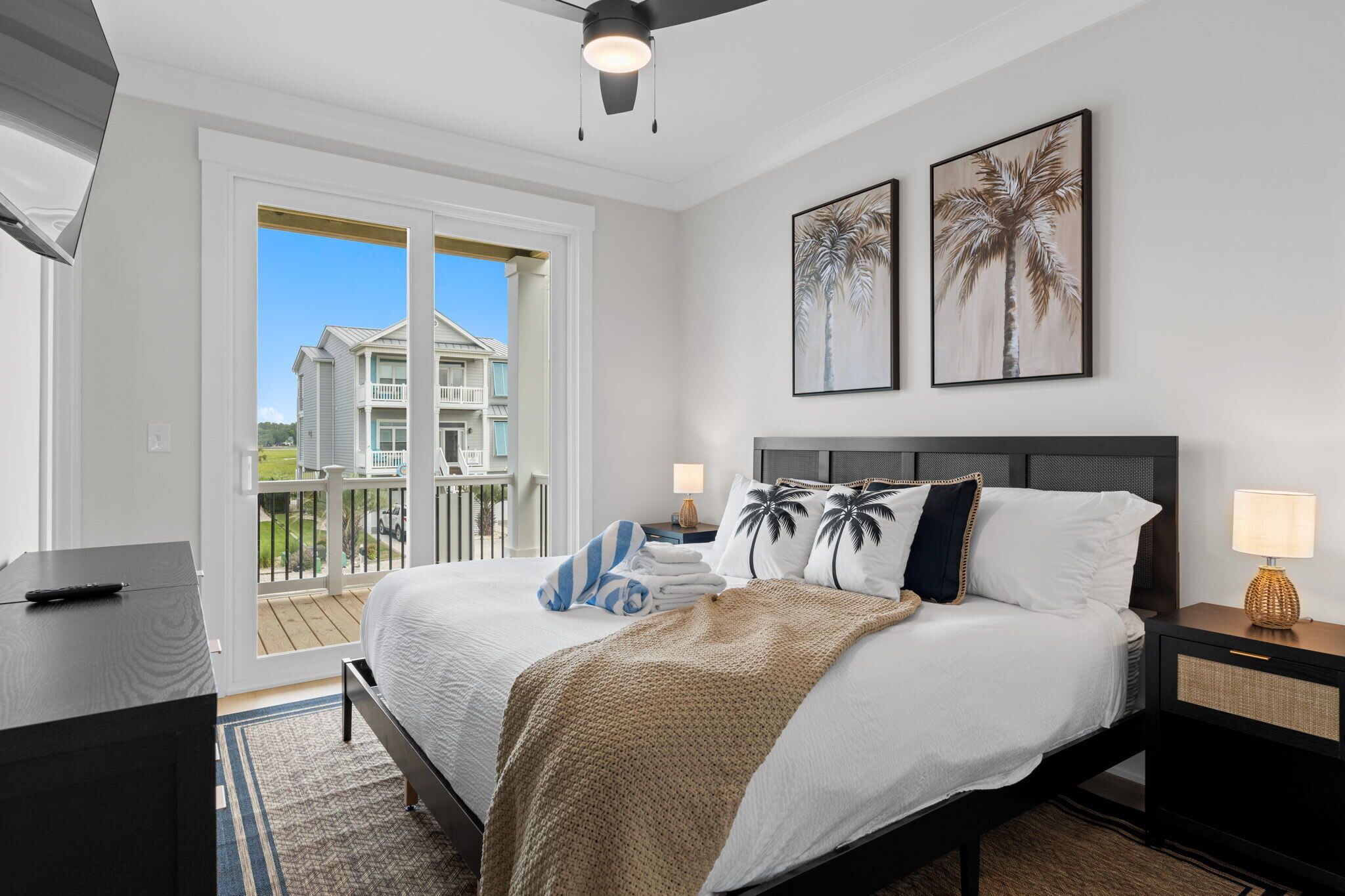 Une chambre à coucher comprenant un lit, une table de chevet, un bureau et un balcon avec vue sur une maison.