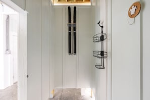 Ein Flur mit einer weißen Tür, einer Holzbalkendecke und einem an der Wand befestigten schwarzen Metallregal.