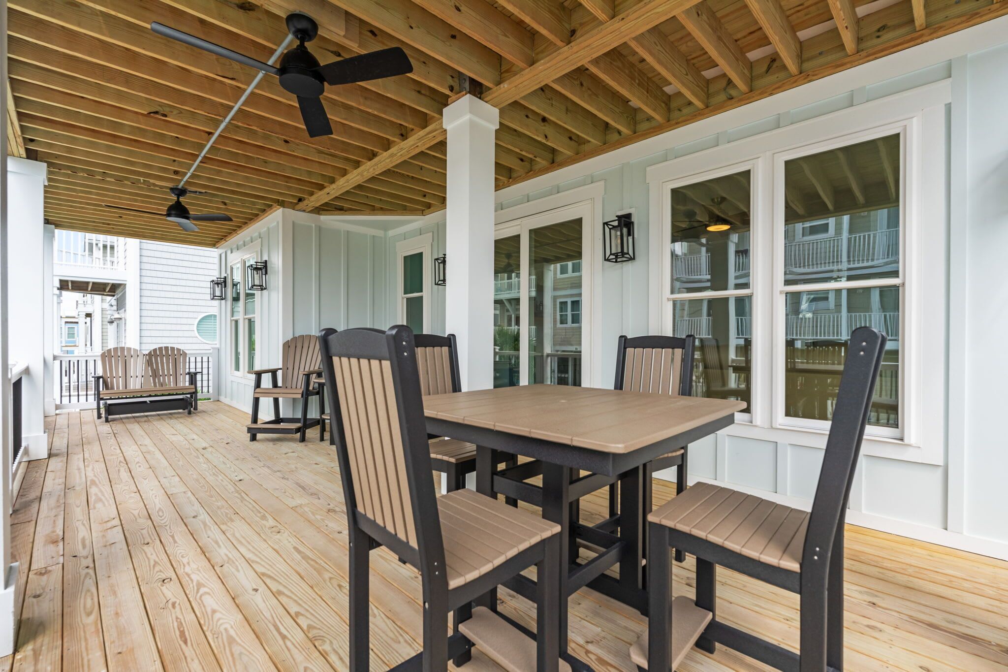 A covered porch with a wooden floor, a table with chairs, and a ceiling fan.