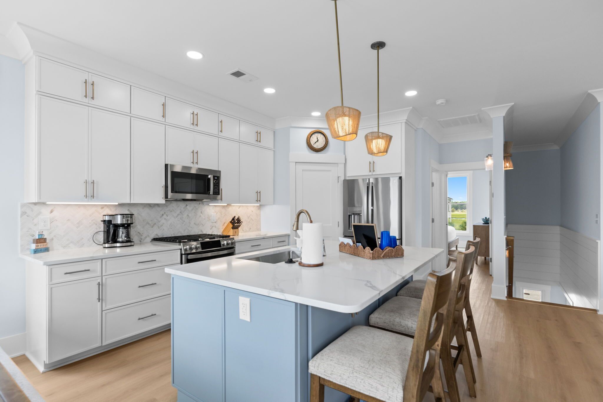 A modern kitchen with white cabinets, a central island, stainless steel appliances, and pendant lighting.